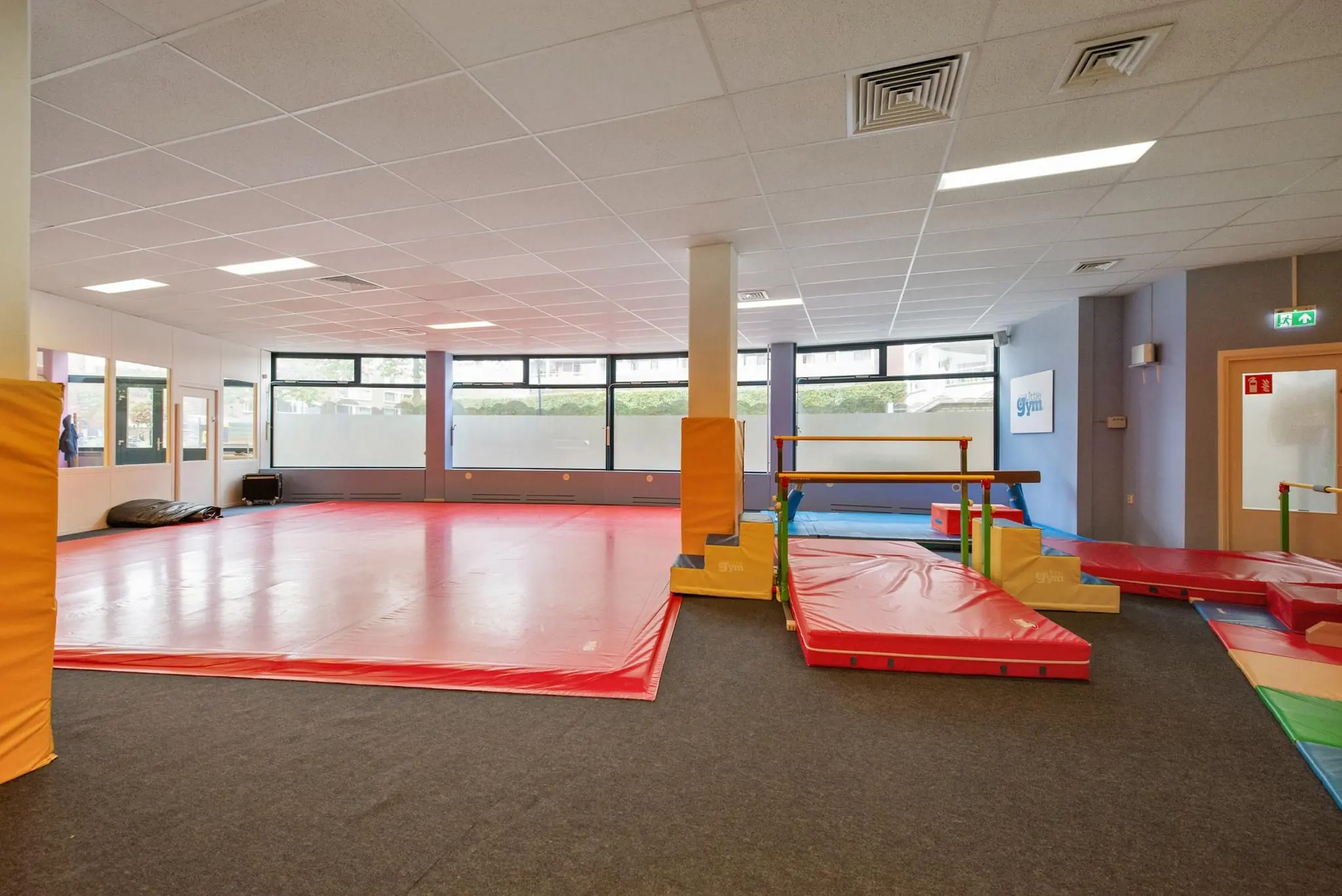 Binnenruimte van een kleurrijke gymzaal aan de Koningin Julianalaan met zachte matten en turntoestellen voor kinderen.